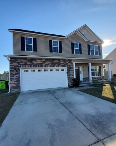 Two-story suburban house with gray siding, stone garage base, white garage door, and front porch, viewed from driveway