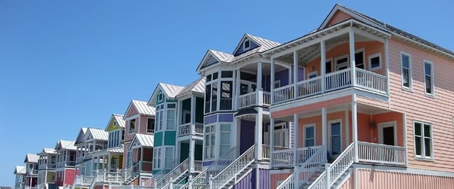 Row of colorful beach houses with white railings and metal roofs on sandy beach under clear blue sky