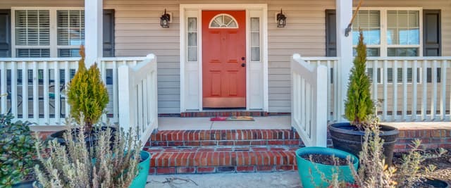 Front porch with red door, white columns, brick steps, and potted plants flanking the entrance