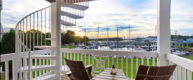 Waterfront deck with Adirondack chairs, spiral staircase, and marina view at sunset