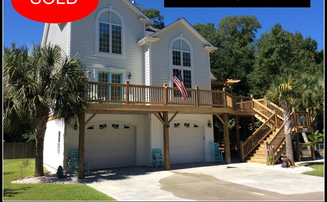 Two-story white house with wooden deck and double garage, palm trees, clear blue sky