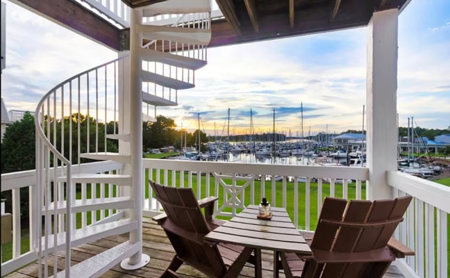 Waterfront deck with Adirondack chairs, spiral staircase, and marina view at sunset